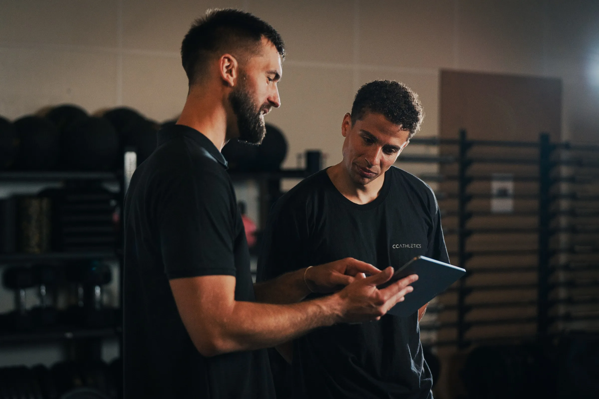 A coach and an athlete standing together in a gym, looking at a test set up on a tablet.