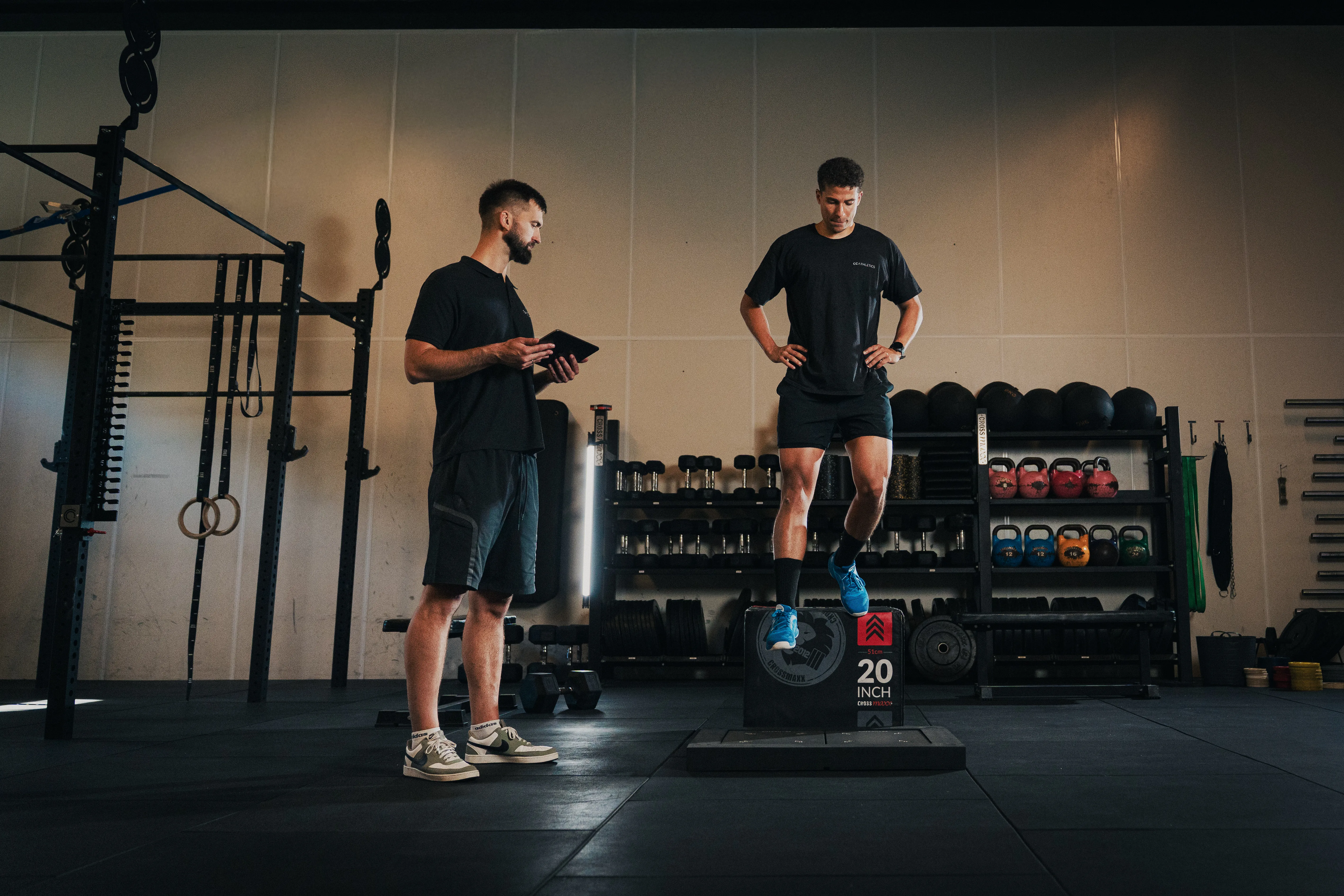 An athlete stepping off a plyo box to perform a drop jump onto a PlateMate force plate while a coach records the result on a tablet