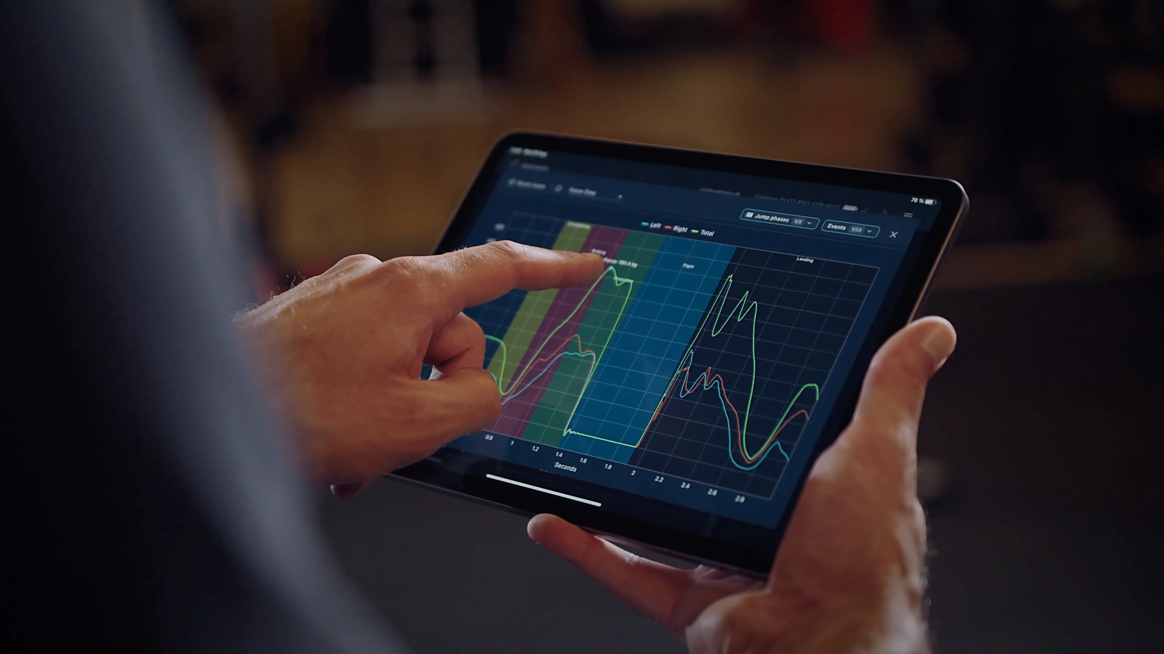 A coach pointing at a countermovement jump force-time curve in the ForceMate app on a tablet, with left, right and total force traces.