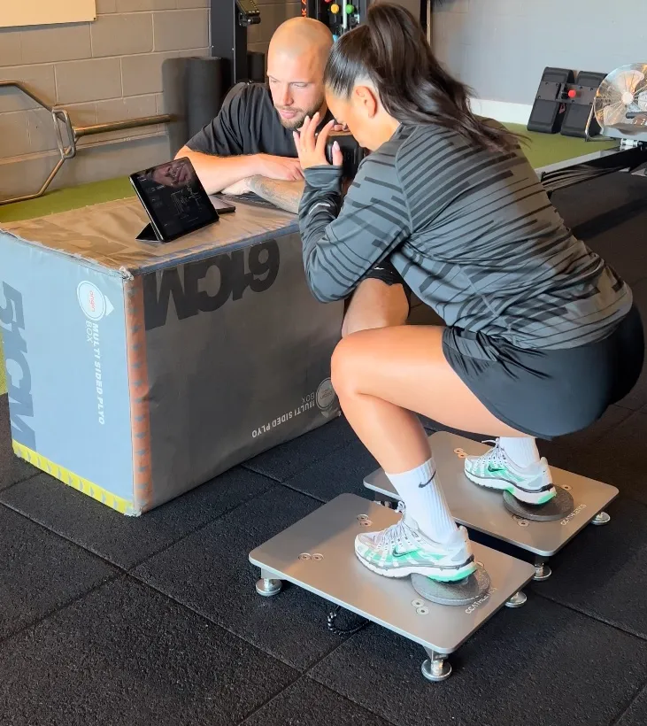 Andrew Henson watching ForceMate on a tablet while a client squats on PlateMate force plates