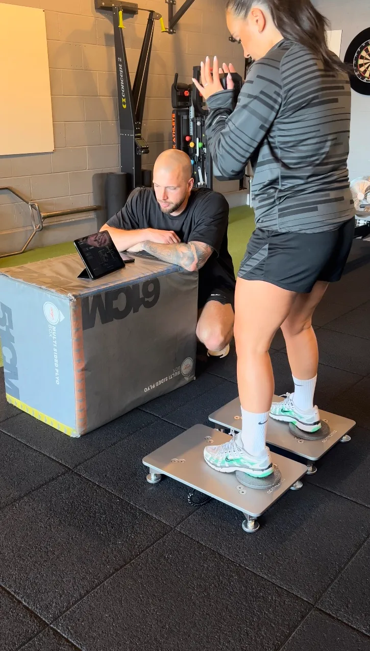 A client standing on two PlateMate force plates while Andrew reviews the live data